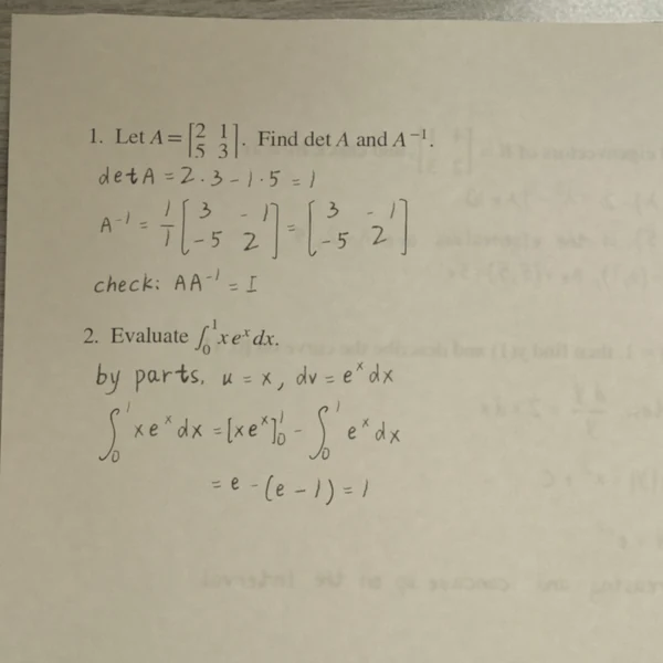 拍照效果的成品：木桌上的一张答题纸，手写的两道英文数学题解答：2×2 矩阵的行列式和逆矩阵，用分部积分算定积分。